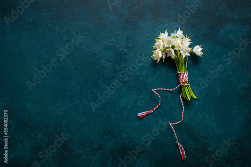 Fresh beautiful bouquet of the first spring forest snowdrops flowers with red and white cord martisor - traditional symbol of the first spring day on blue background