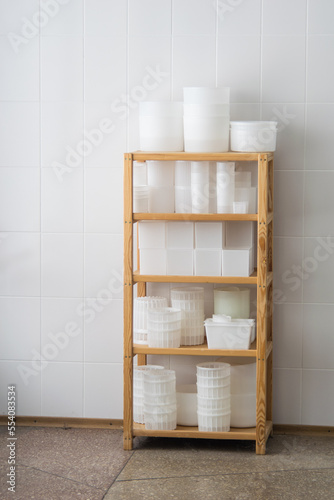 White plastic cheese forms, molding glasses on wooden shelves. Private small-scale cheese factory