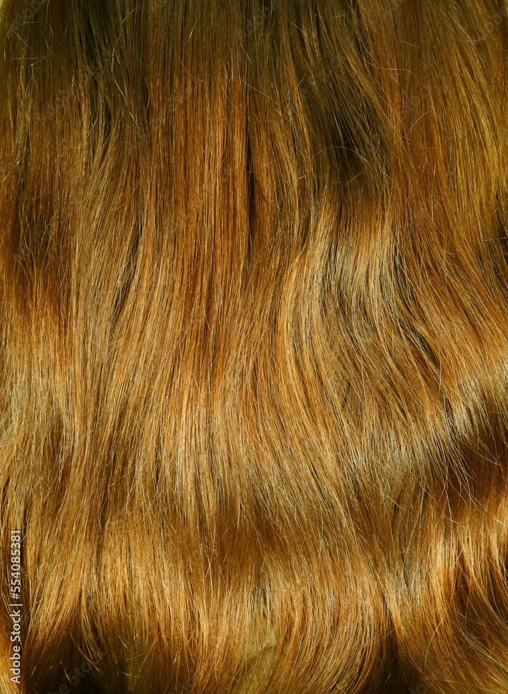 Naklejka premium Hair texture close up golden brown honey color, closeup view of bunch of shiny straight brown hair in wavy curved style.