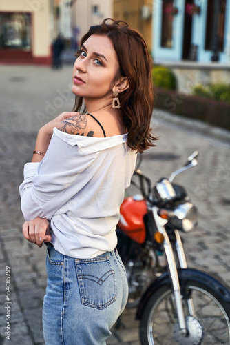Obraz na płótnie Young beautiful woman shows her bare shoulder with a tattoo standing by a bike on the street w salonie