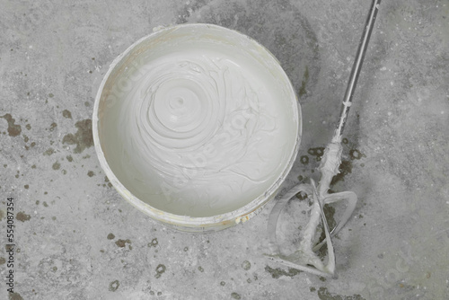 Bucket with plaster and power mixer on concrete floor, flat lay