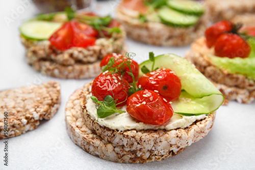 Crunchy buckwheat cakes with cream cheese, tomatoes and cucumber slices on white table, closeup