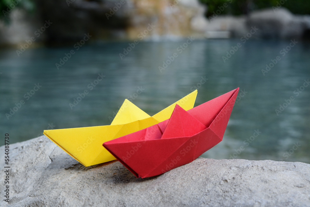 Beautiful yellow and red paper boats on stone near pond, closeup