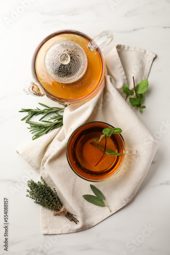 Aromatic herbal tea with rosemary, sage, thyme and mint on white marble table, flat lay