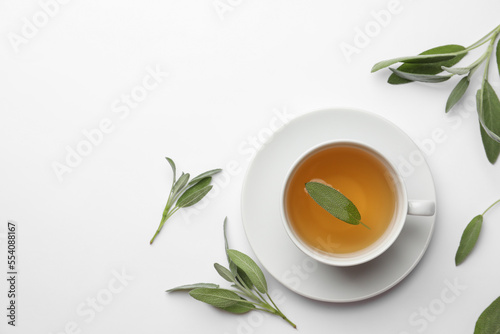 Cup of aromatic herbal tea with sage on white table, flat lay. Space for text