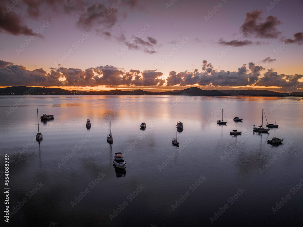 Naklejka premium Aerial sunrise waterscape with boats, clouds and reflections