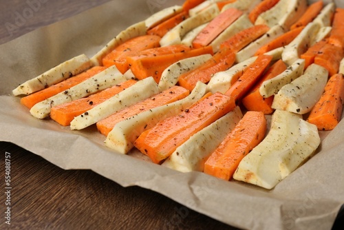 Baking tray with parchment, parsnips and carrots on wooden table, closeup