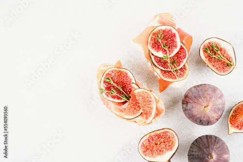 Healthy quick breakfast - toasts with fresh ripe fig, cheese, prosciutto and herbs over white concrete table background with copy space. Top view, selective focus