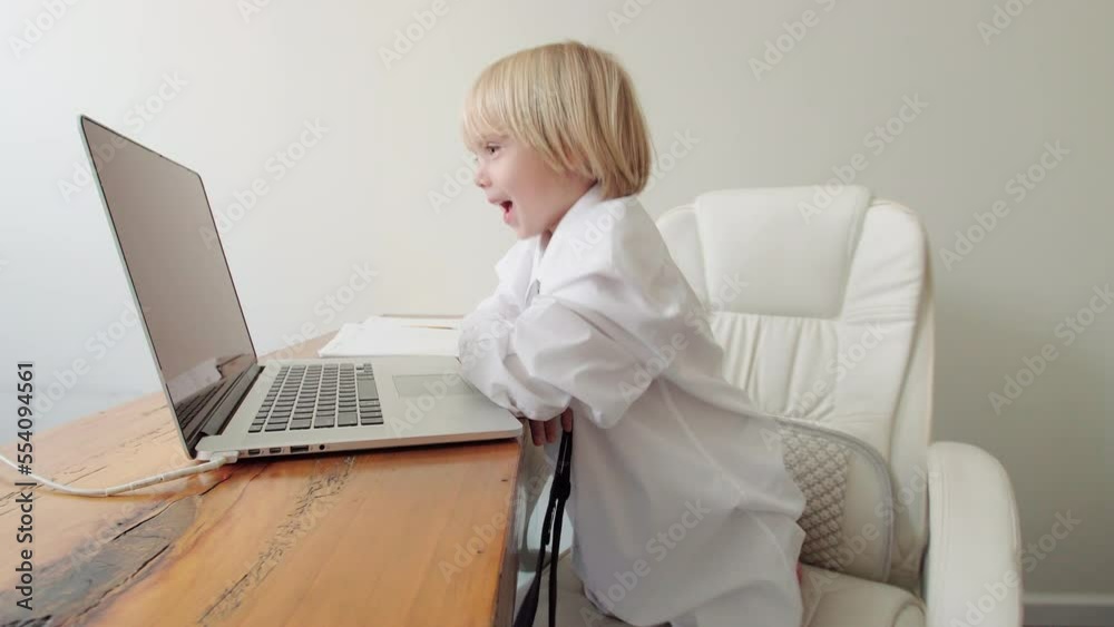 Adorable caucasian 5 years old boy in his fathers's shirt and tie is writing down something in his notebook at home office in front of the laptop. Funny moment of a boy pretending to be an adult Adorable caucasian 5 years old boy in his fathers's shirt and tie is writing down something in his notebook at home office in front of the laptop. Funny moment of a boy pretending to be an adult