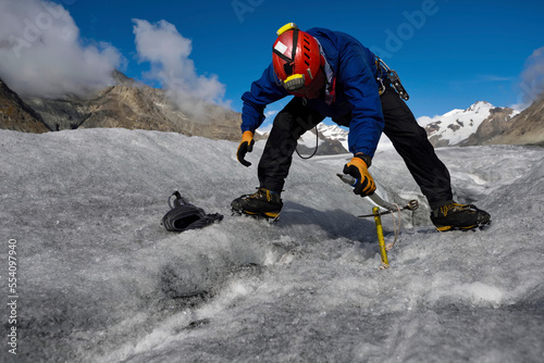 An expedition leader fixing an ice screw to anchor a rope before descending down into a moulin. photo
