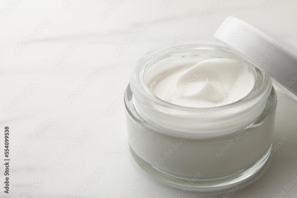 Glass jar of face cream on white marble table, closeup. Space for text Glass jar of face cream on white marble table, closeup. Space for text
