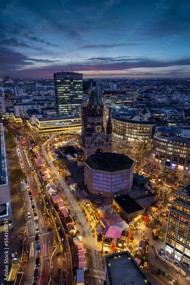 Fototapeta premium Elevated view of the illuminated Breitscheidplatz in Berlin, Germany, with the Kaiser Wilhelm Memorial church and a Christmas Market during winter dusk time