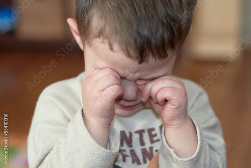 crying little boy is rubbing his eyes