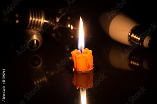 Switched off light or not glowing light bulb near a burning candles in total darkness.