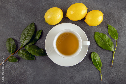 A cup of green tea, tea leaves and lemons, on dark background
