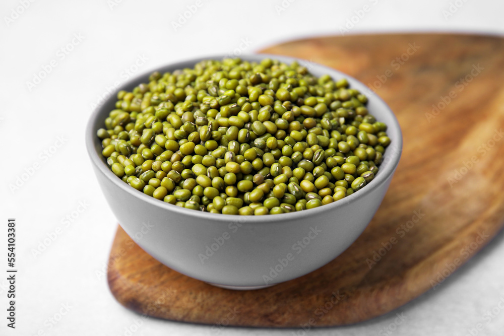 Bowl with green mung beans and wooden board on white table, closeup Bowl with green mung beans and wooden board on white table, closeup