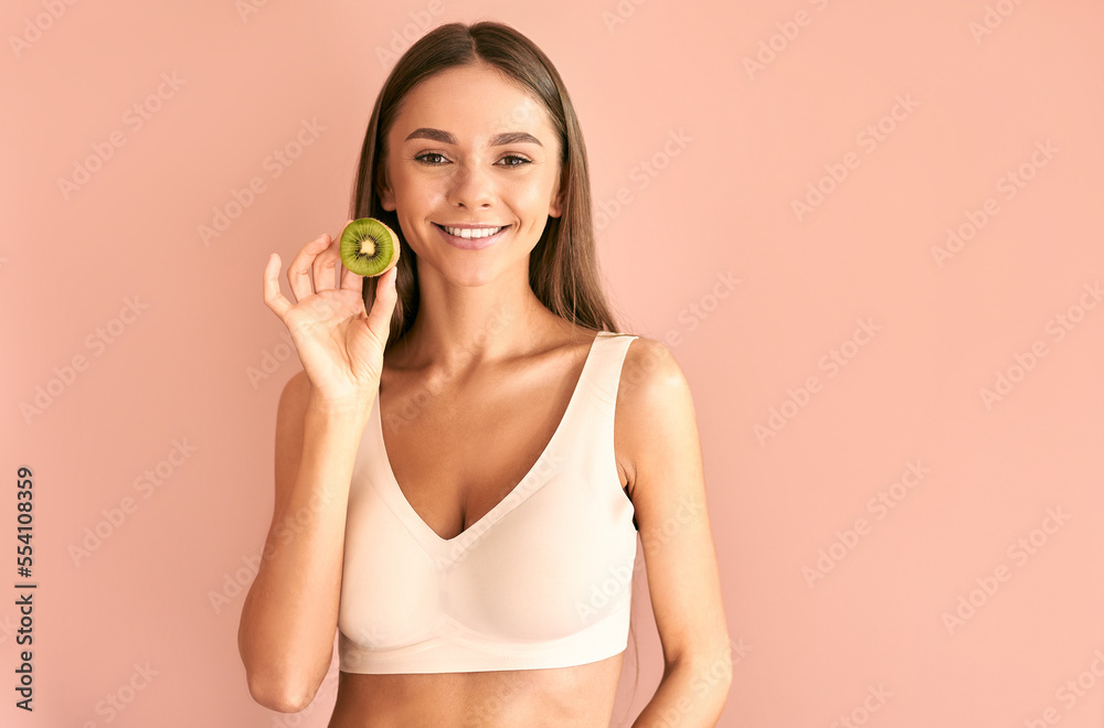 Portrait of a beautiful brunette woman wearing a white bra holding a kiwi and looking at the camera. Portrait of a beautiful brunette woman wearing a white bra holding a kiwi and looking at the camera.