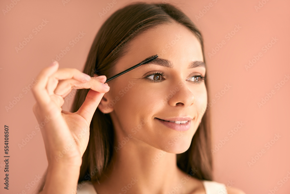 Portrait of a beautiful young woman on a beige background combing her eyebrows. Eyebrow care. Portrait of a beautiful young woman on a beige background combing her eyebrows. Eyebrow care.