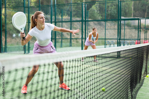 Woman in shorts playing padel tennis on court. Racket sport training outdoors. © JackF