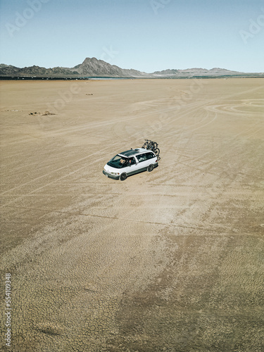 Aerial view of self converted camper van recreational vehicle driving on a dry lake bed in the desert of southern nevada United States with solar panels and bikes mounted to the rv van life rig.