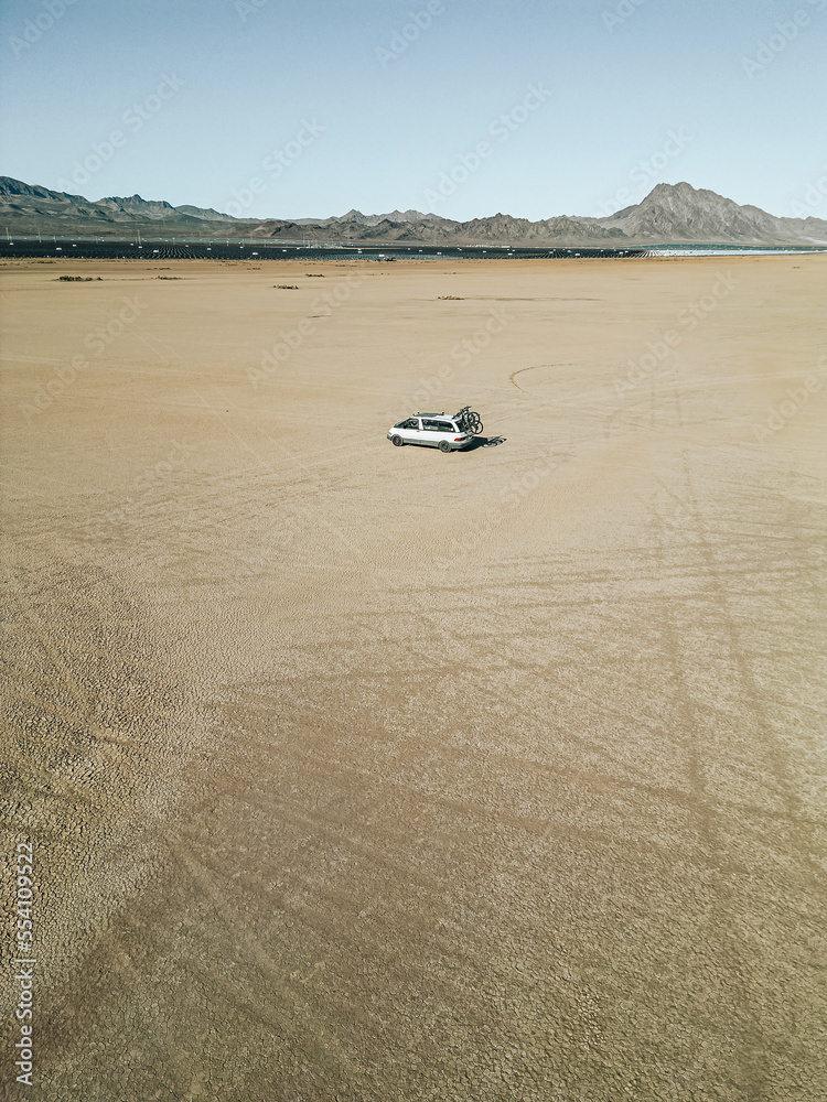 Obraz premium Aerial view of self converted camper van recreational vehicle driving on a dry lake bed in the desert of southern nevada United States with solar panels and bikes mounted to the rv van life rig.
