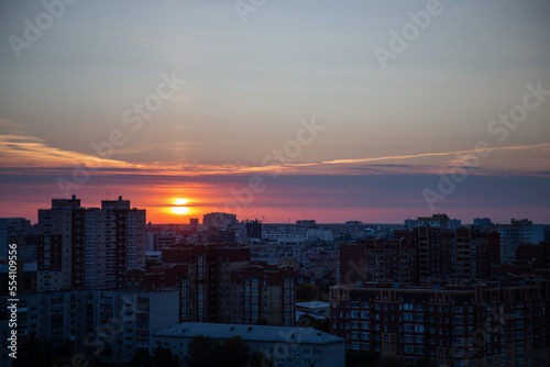 Orange sunset hides behind residential area buildings in evening city. Sunlight sends last rays to illuminate city and signals about upcoming night © SlavaStock