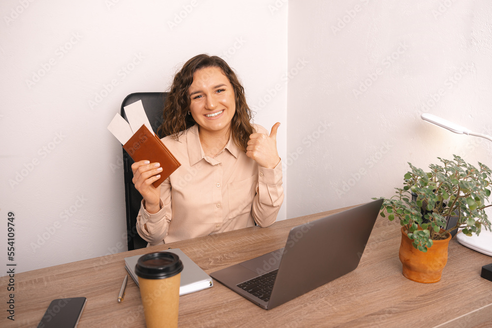 Wide smiling woman has just booked her flight online and she recommends it. She is sitting in the office in front of her laptop showing thumb up. Wide smiling woman has just booked her flight online and she recommends it. She is sitting in the office in front of her laptop showing thumb up.