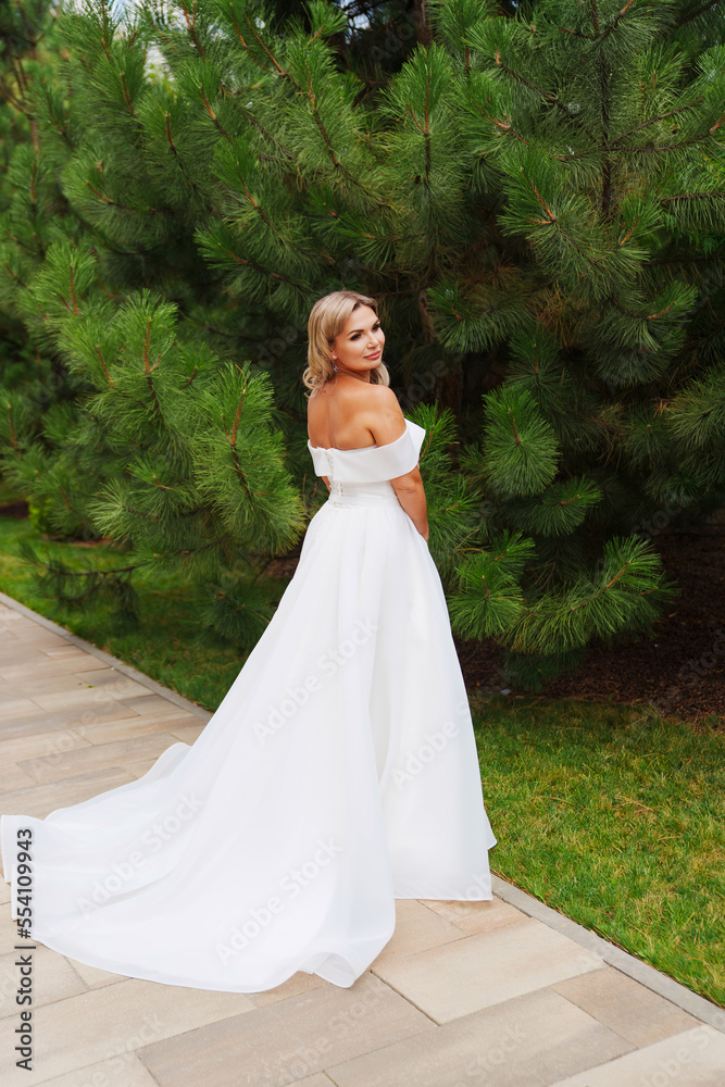 a blonde bride on a path in the park in a white long dress. a blonde bride on a path in the park in a white long dress.