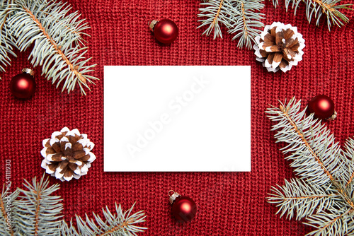 Christmas greeting card mockup, fir tree branches and holiday decorations on red knitted sweater background, top view, flat lay. Blank New Year card with winter decor
