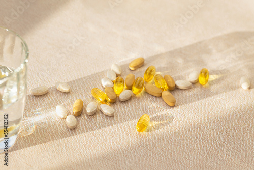 Pills and a glass of water on pastel background with shadow. Health care concept. Supplements and vitamins. Selective focus