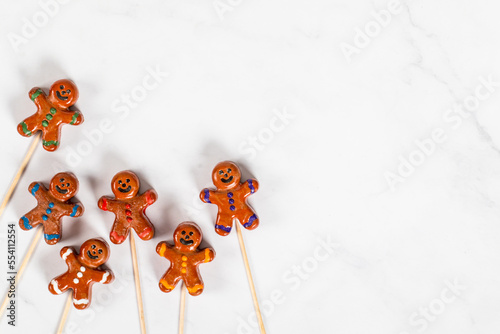 Christmas cookie in the form of a gingerbread man, covered with colored caramel and icing sugar, on a wooden stick. White background. Top view. Copy space