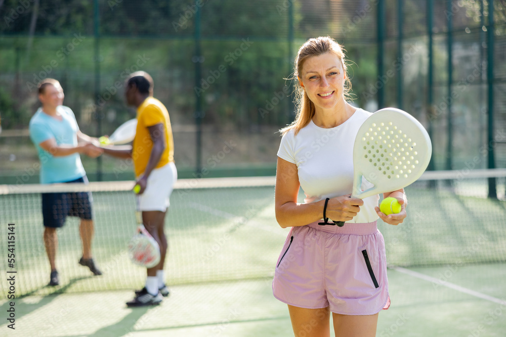 Happy woman posing with racket and ball in hands on padel court