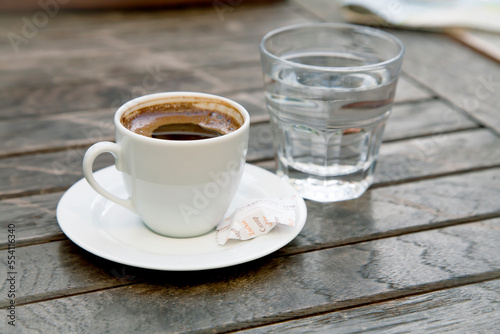 Small cap of strong coffee espresso with glass of clean water on wooden table.