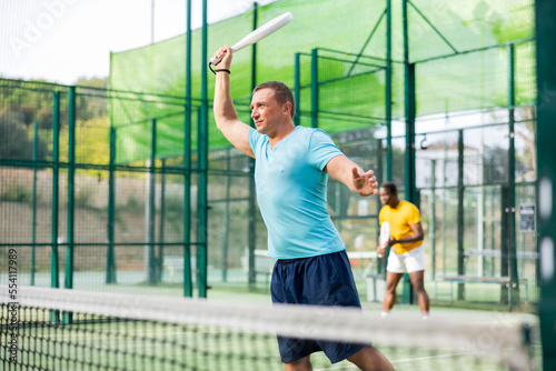 Caucasian man in sportswear playing padel tennis match during training on court.