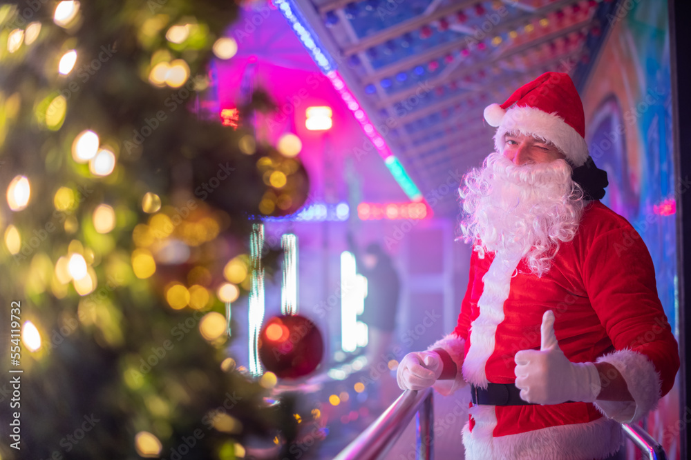 Portrait von einem verkleideten Weihnachtsmann, der auf einem Weihnachtsmarkt von Bokeh von bunten Lichtern umgeben ist