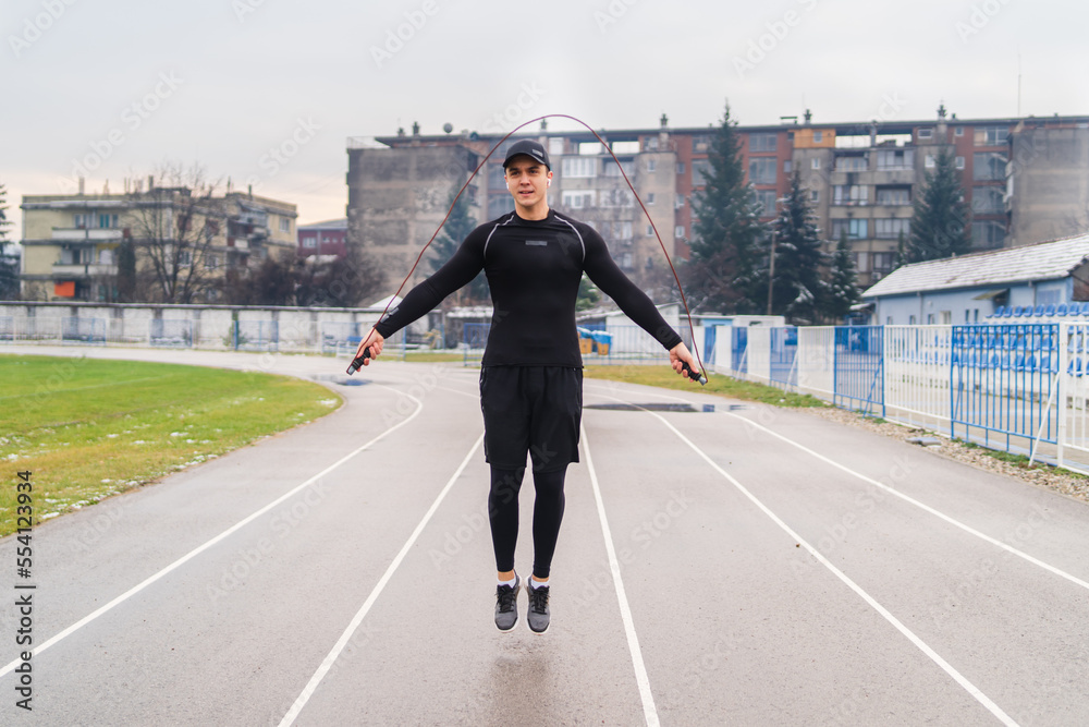 A young man training running stretching jumping a rope on the stadium early in the cold morning A young man training running stretching jumping a rope on the stadium early in the cold morning
