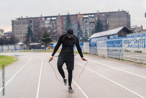 A young man training running stretching jumping a rope on the stadium early in the cold morning 