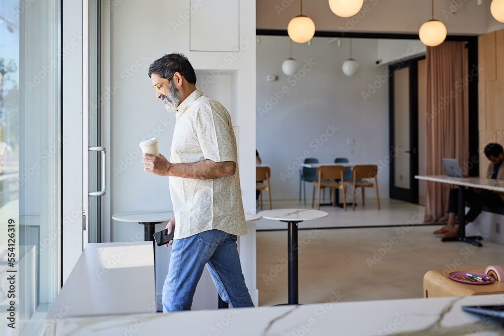 Smiling mature man with disposable coffee cup leaving coffee shop Smiling mature man with disposable coffee cup leaving coffee shop