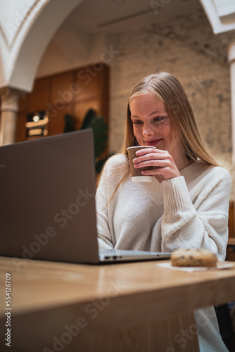 Young woman is working hard with her computer while is drinking a coffee at a cafeteria