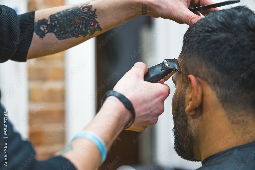 Naklejka premium Close up of barber hands using hair clipper for a male haircut. High quality photo