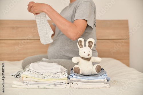 Pile of baby clothes and pregnant woman on a bed photo