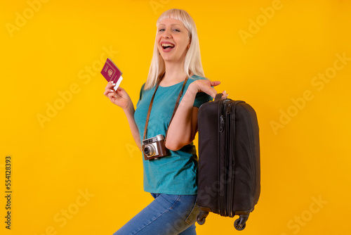 Portrait of tourist with suitcase, travel, vacation, blonde caucasian girl on yellow background studio