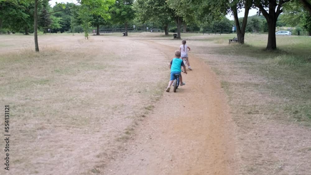 Sport activity for children. Small kids playing bicycle and scooter riding on path in park in summer drought dry grass. Little Brother and Sister Siblings playing together. Child development concept Sport activity for children. Small kids playing bicycle and scooter riding on path in park in summer drought dry grass. Little Brother and Sister Siblings playing together. Child development concept
