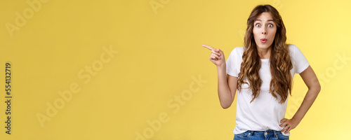 Wow incredible lets click. Impressed surprised pretty european woman long curly hairstyle folding lips intrigued stare astonished wondered awesome cool promo offer pointing left yellow background