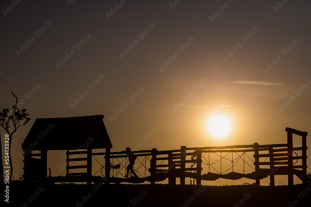 Silhouette of a kid playing on a playground at sunset in Ecoparque park, Caxias do Sul, RS, Brazi Silhouette of a kid playing on a playground at sunset in Ecoparque park, Caxias do Sul, RS, Brazi