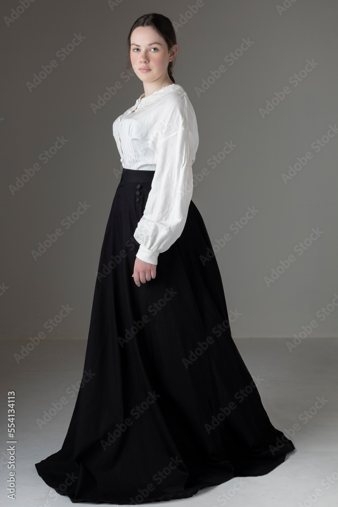 A young Victorian or Edwardian woman wearing a white linen Garibaldi blouse and a black skirt against a studio backdrop