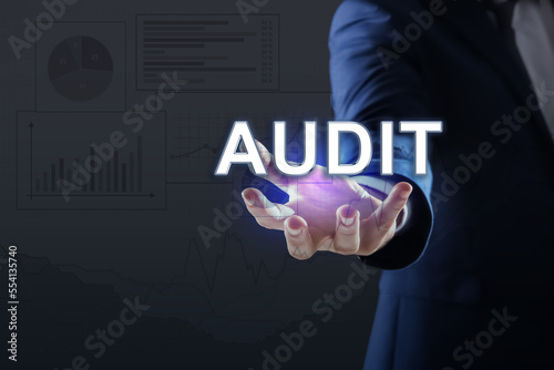 Audit concept. Businessman holding digital word in hand on dark background, closeup. Graphs and charts © New Africa