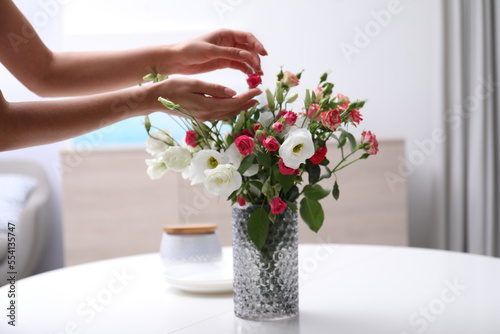 Fototapeta Naklejka Na Ścianę i Meble -  Woman and vase with beautiful flowers on white table in room, closeup