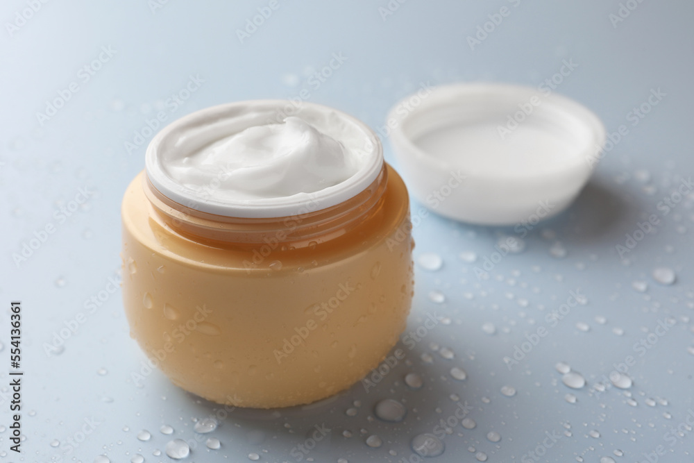 Jar of face cream on light blue surface covered with water drops, space for text Jar of face cream on light blue surface covered with water drops, space for text