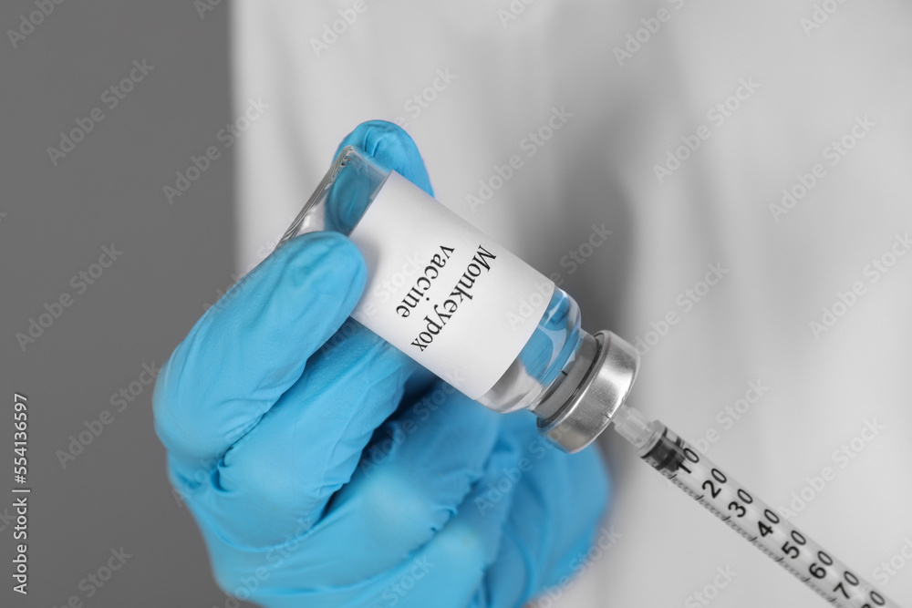 Nurse filling syringe with monkeypox vaccine from glass vial on grey background, closeup Nurse filling syringe with monkeypox vaccine from glass vial on grey background, closeup